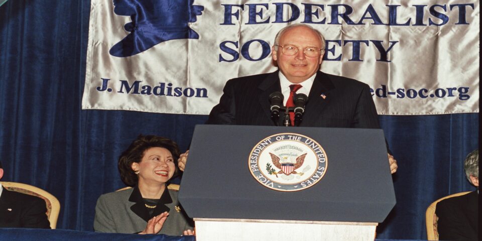 A white male speaker stands in front of a Federalist Society banner at a podium, decorated with the seal of the Vice President of the United States, at a Federalist Society Convention and Republican Attorneys General Dinner held in Washington D.C. in 1992. The speaker looks to their left as they grip the podium.